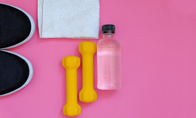 Fitness concept with dumbbells, bottle of water, towel and sneakers on pink background with copy-space from top