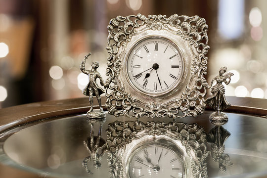 Silver clock on the background bokeh. Vintage metal watch with male and female figures. 