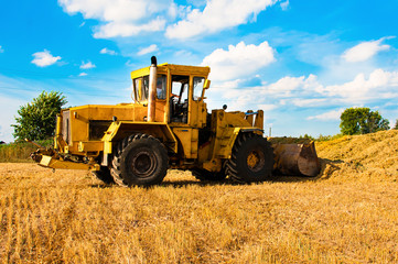 Yellow bulldozer in a field at harvest on a Sunny day