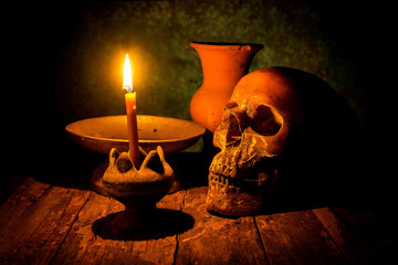 Skull and candle with candlestick on wooden background, still li