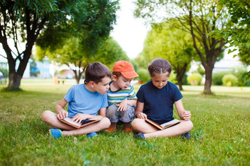 Fototapeta premium kids in the park reading books together. three children to read and consider the illustrations in books. kids sitting in the park on the grass