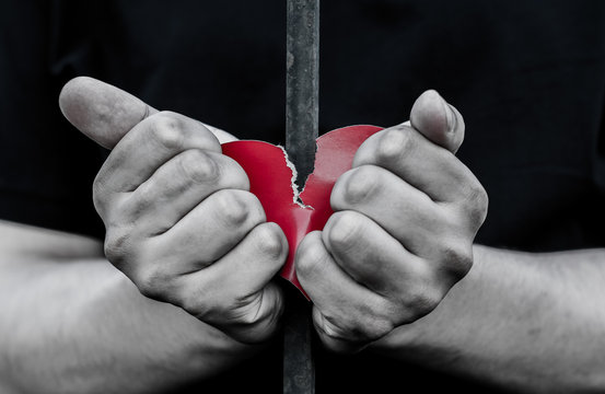 Teenager standing behind iron bars. Two hands holding a heart made out of paper.
