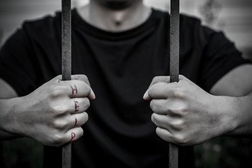 Man held with two hands for metal bars. On the fingers of one hand is written "help."
