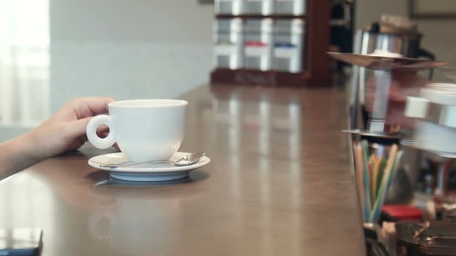 Waitress serving coffee to a man on a mobile phone passing the cup over the counter as he texts a message, close up of the hands