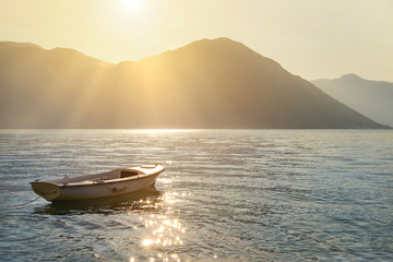 Fishing boat at sea against sunset mountains with sun rays