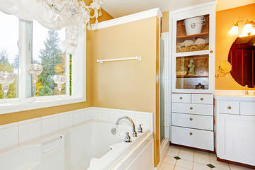 Yellow bathroom with white storage combination and elegant chandelier.