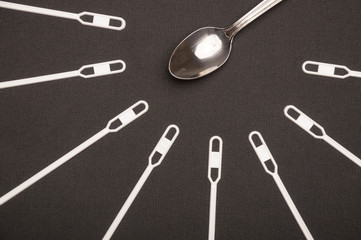 White stirring sticks lying around metal teaspoon on black background. Fast food against homemade...