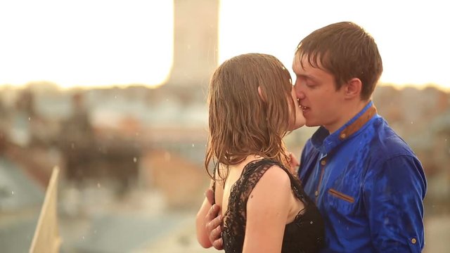 Young loving couple kissing on the rooftop of ancient city building while raining