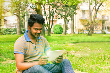 Fototapeta premium Young indian man having video call on tablet in park university