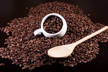 Cup full of coffee beans and a wooden spoon on a dark background