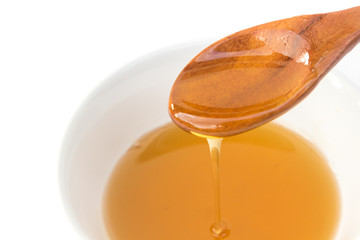 Closeup honey dripping from a wood spoon to bowl on white background, Healthy and beauty spa concept