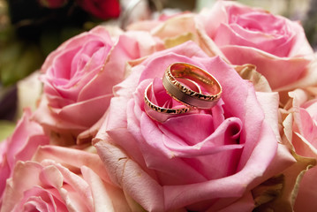 Złote obrączki ślubne na bukiecie różowych róż 