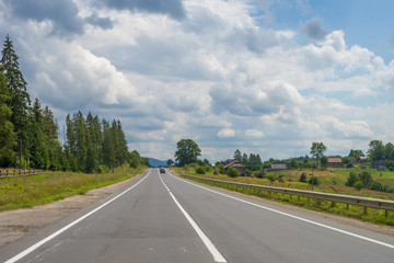 Summer day landscape with road, cloudy sky and small houses. Ukraine, Carpathian. 
