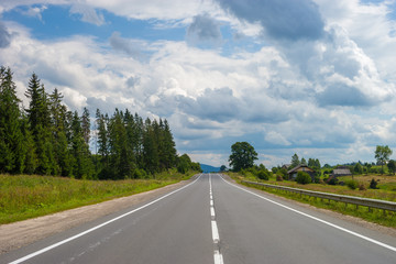 Summer day landscape with road, cloudy sky and small houses. Ukraine, Carpathian. 