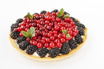 Delicious mini tart with fresh red currants, blackberries, raspberries, strawberries and cream on white background.