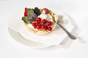 Delicious mini tart with fresh red currants, blackberries, raspberries, strawberries and cream on white plate.