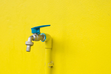 Closeup faucet on concrete Yellow wall background. Water leaking