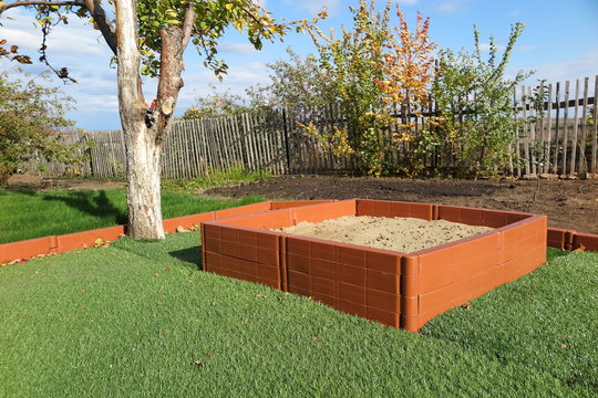 Modern plastic sanbox on the artificial lawn in the sunny autumn garden