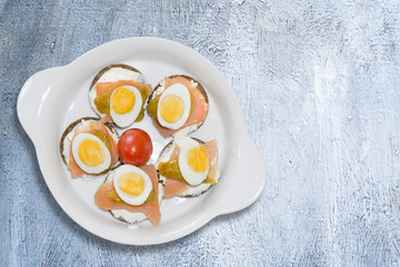 Mini sandwiches with dark bread with salmon eggs and yogurt on white ceramic plate. View from above.