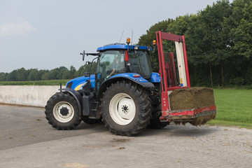 Blue tractor with a red bale slicer.