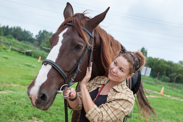 Fototapeta premium Happy smiling young beautiful woman is near a chestnut horse