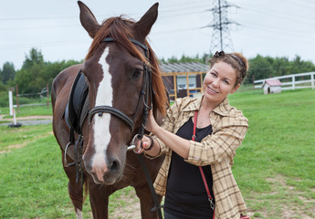 Fototapeta premium Attractive joyful horsewoman holding chestnut horse