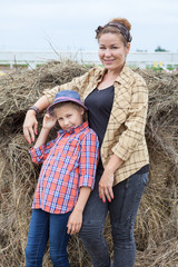 Naklejka na ściany i meble Caucasian mother and her little daughter wearing in shirts standing next to a stack of hay