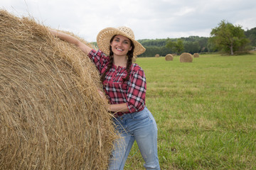 Naklejka na ściany i meble Portrait of young woman standing next to a stack of hay in sunlight