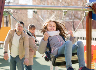 family with two girls having fun on swings outdoors