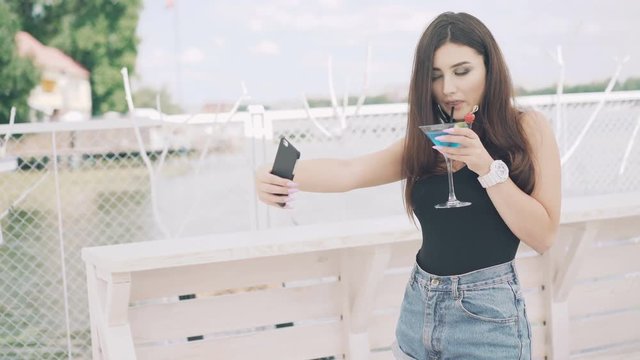 Young woman taking selfie with goblet of blue cocktail on the beach in 4K