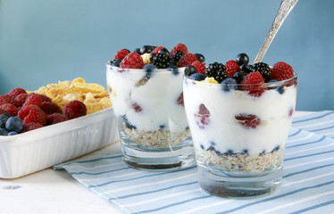 Light breakfast for two. Plate full of fruits and cereals, two glasses of dessert with yogurt, oatmeal, fruit and cornflakes. Rustic wooden table