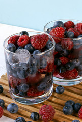 Cooled by ice juicy summer berries in glasses: raspberries, blueberries, bilberries. Rustic white table. Close view. 