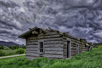 Old abandon log home outside of Yampa Colorado with a building storm in the sky.