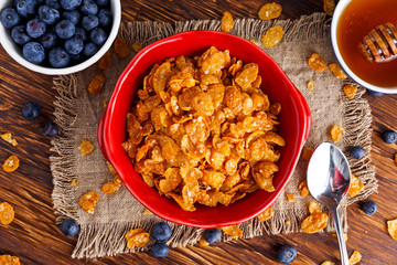 Corn Flakes with berries raspberries, blueberries, glass of milk, and sweet honey.