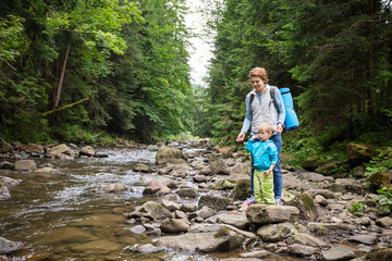 Mother and son resting by a stream in mountains. The boy throwing stones in water.
