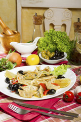 Prepared cod pieces in sauce, cherry tomatoes, black olives and lemon served on a white plate.