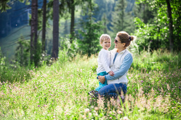 Happy young woman and toddler son on sunny meadow in mountains