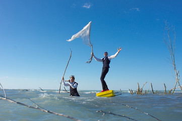 Two men in suits with a yellow suitcase and white flag, in an unusual journey through the ocean.