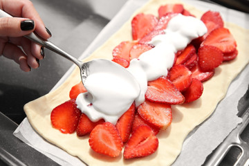 Female hand pouring cream on strawberry dessert in oven tray