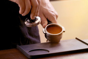 Barista pressing ground coffee with tamper in portafilter