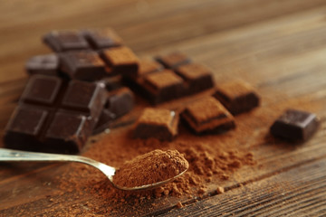Spoon full of cocoa powder and chocolate pieces on wooden background