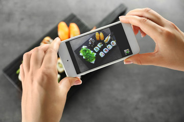 Female hands taking photo of sushi roll set with phone