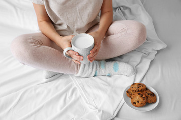 Woman having breakfast with cookies and cup of milk on the bed, close up