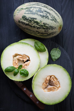 Top view of sliced and whole melons on a black wooden surface