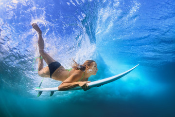 Young active girl in bikini in action - surfer with surf board dive underwater under breaking big...