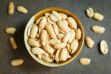 Roasted peeled salted peanuts in rustic bowl on wooden background (focus on peanut in bowl)