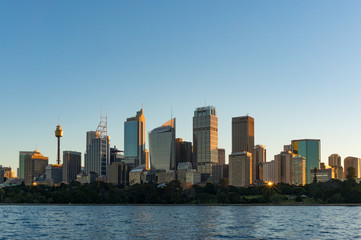 Fototapeta na wymiar Sydney CBD skyscrapers with Sydney Tower and Royal Botanic Garden view on sunset with sun reflecting from windows. Modern urban cityscape with office buildings