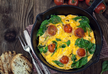 Spinach frittata with cherry tomato in iron skillet 