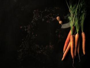 Raw carrot with green leaves and knife on an old metal tray, top view, copy space, toned