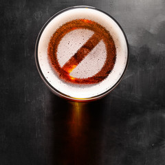 forbidden symbol on foam in beer glass on black table, view from above
